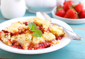 crumble with strawberries in white plate on a blue background