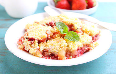 crumble with strawberries in white plate on a blue background