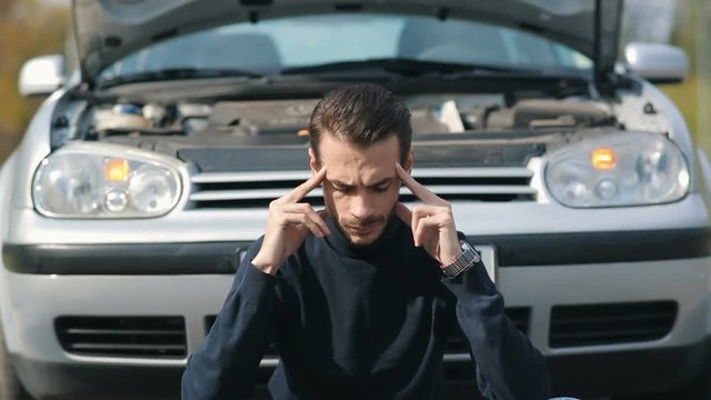 Man with headache in a front of broken car