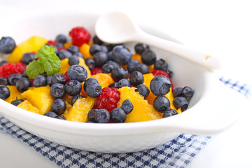 fresh berries in a white plate on a white background: raspberries, blueberries, peach.