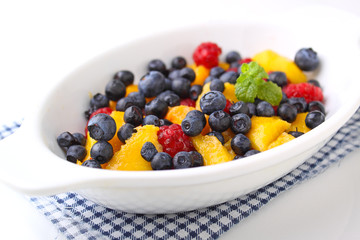 fresh berries in a white plate on a white background: raspberries, blueberries, peach.