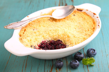 crumble with blueberry, bilberry in white plate on a blue background.