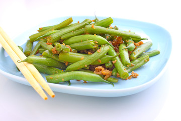 green beans with minced meat and garlic in a blue bowl on a white background