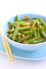 green beans with minced meat and garlic in a blue bowl on a white background