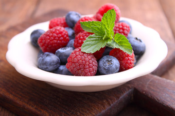 healthy breakfast. raspberries and blueberries in a white bowl on a wooden background.