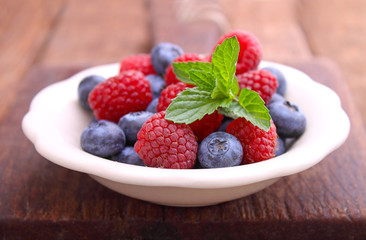 healthy breakfast. raspberries and blueberries in a white bowl on a wooden background.
