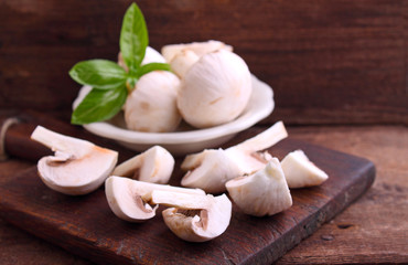 Champignon mushrooms cut into slices on old wooden board