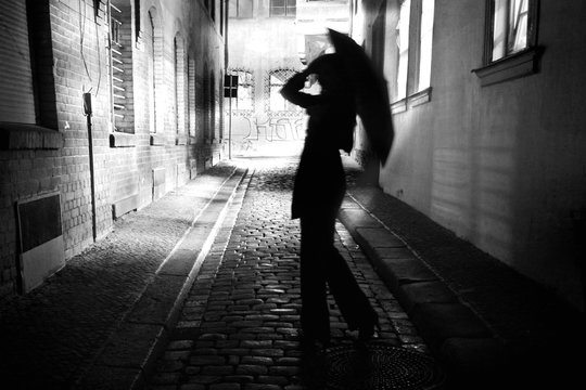 Frau mit Regenschirm läuft durch eine dunkle enge Gasse bei Nacht