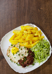 Grilled Beef Steak with fried egg, vegetables salad and potato in a white plate on wooden table