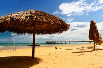 Palm umbrellas on the beach and pier in background in Francavill