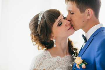 Bride and groom in studio light stand kiss on a white background