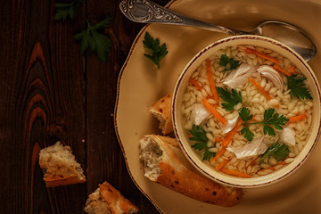 Chicken soup with pasta on a dark wooden background.
