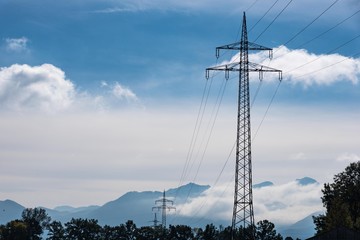 Strommast im Gegenlicht mit Bergen, Himmel und Wolken