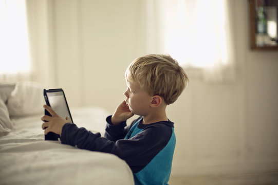 Young boy looking serious as he plays with a portable information device.