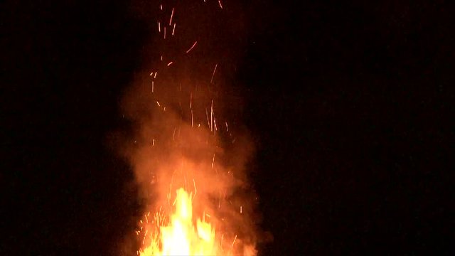 Large fire burning at night with smoke and sparks rising.