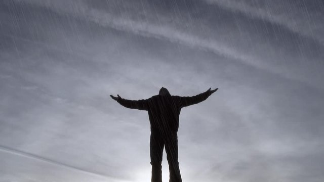Model released, silhouette of man spreading his arms, praising the Gods as it pours down rain.