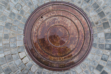 Closeup photo of Old Sewer rust manhole cover on the urban asphalt road. Rain scene.