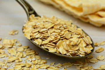Old fashioned whole grain rolled oats with vintage silver spoon on rustic wood with yellow napkin in background.  Shallow DOF with focus on foreground oats and rim of spoon.