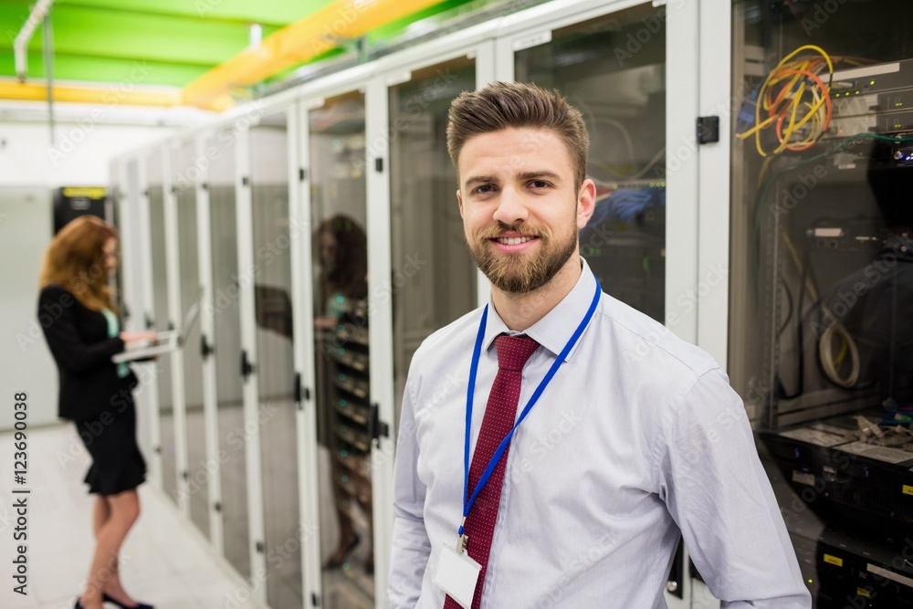 Poster smiling technician standing in a server room