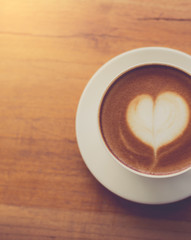A cup of coffee with heart pattern in a white cup on wooden back