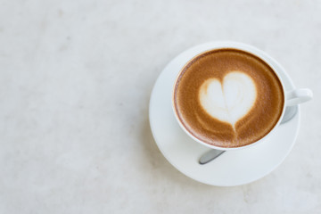 A cup of coffee with heart pattern in a white cup on wooden back