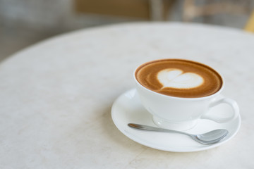 A cup of coffee with heart pattern in a white cup on wooden back