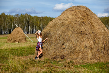 Young blonde country girl in hat near haystack