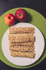 Roasted rolled pancakes on a white round plate and two apples near. Top view . Flat lay