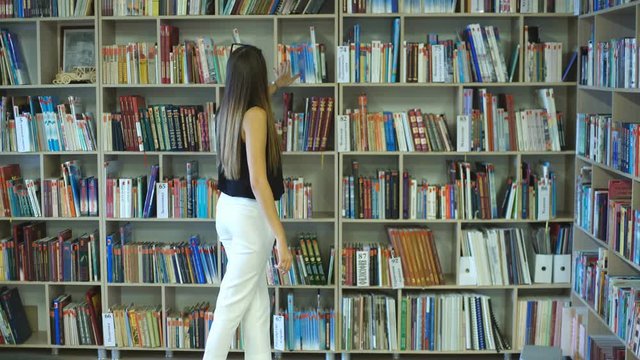 student girl chooses among the shelves of a book in the library