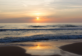 Fototapeta na wymiar Golden wave on a sandy beach at sunrise. Ocean sunrise on a quiet morning.