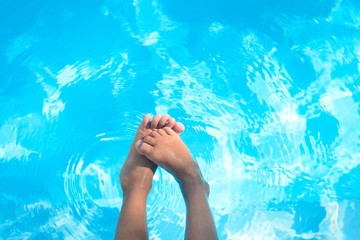 Child bare feet above blue water in swimming pool