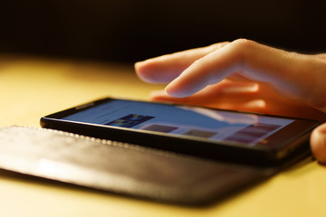 Human hand using smartphone. Finger swipe up and down the screen of smartphone. Warm light. Shallow focus.