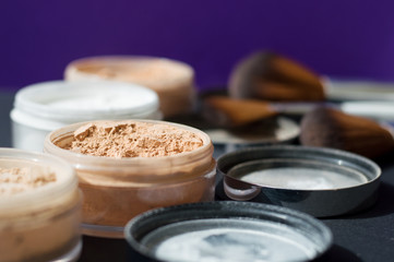 Collection of beauty boxes with mineral powder and make up brushes on purple background