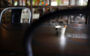 Small iron bucket.Metal ashtray with a cigarette on rustic table ,very shallow depth of field and...