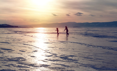 Fototapeta premium Silhouette of two ice skating people at lake Baikal frozen surface on sunset. Winter tourism concept