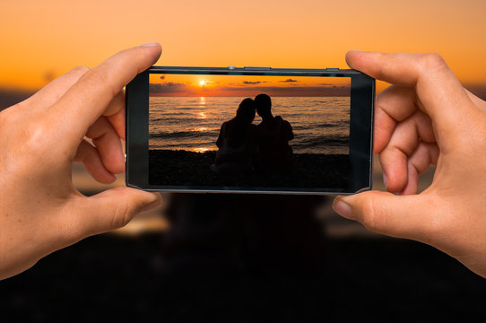 Taking photo of loving couple at sunset with mobile phone
