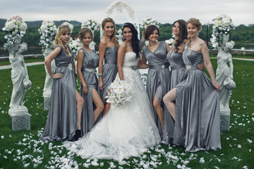 The smiling bridesmaids and bride stand near statuette with flow