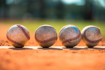 Four well used baseballs on Pitchers Mound with red dirt and outfield in background