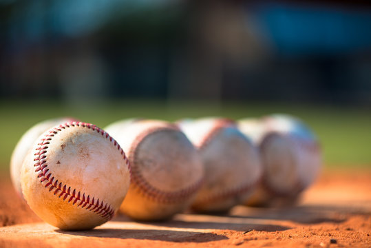 Several well-worn baseballs close up on pitchers mound with empty field in background
