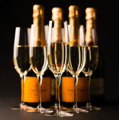 Five sparkling champagne filled glasses flutes with Bottles isolated on Black background for use...