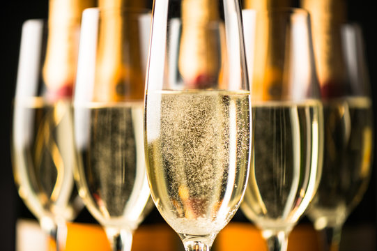 Sparkling champagne glasses flutes close up with bottles in dark background