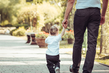 Rear view of father and son holding hands while walking - obrazy, fototapety, plakaty