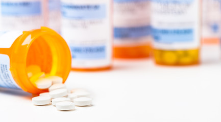 Fototapeta Round white prescription medication medicine pill tablets spilling from a bottle with numerous full bottles in background obraz