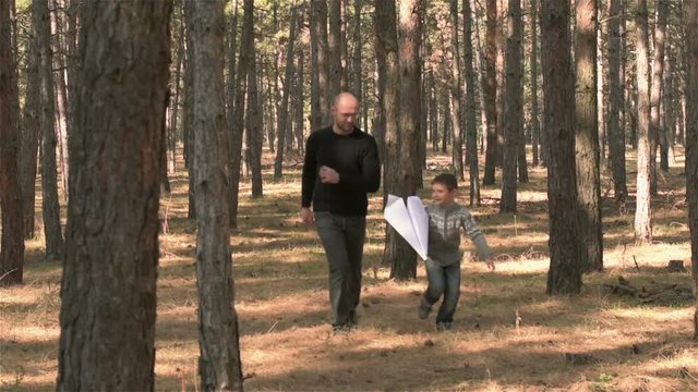 Father and son running through woods with paper airplane