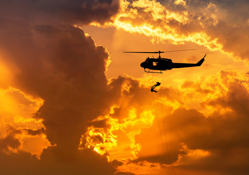    silhouette soldiers in action rappelling climb down from helicopter with military mission counter terrorism assault training on sunset background 