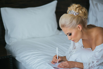 Awesome bride lies on a white pillow while writing a wedding spe - Powered by Adobe