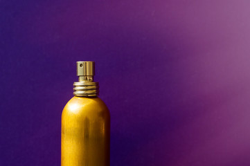 One spray bottle of golden color on purple background. Female perfume