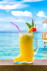 Maldivian cocktail in a glass shoe on background of ocean and bungalow