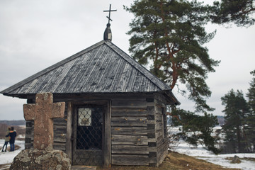 Old stone cross stands in the front of old wooden chapel