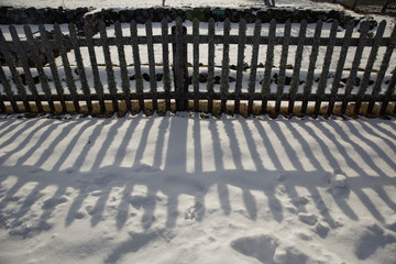 Low wooden fence lies a shadow on the snow
